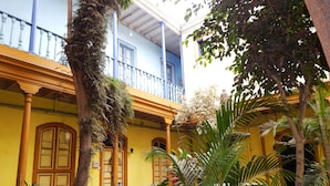 Un patio con edificios amarillos, una fuente y diversas plantas.