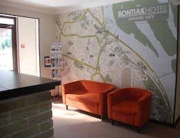 Un vestíbulo de hotel con un mapa grande en la pared, dos sillones naranjas, un mostrador de recepción y una pared de ladrillo.