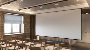 Un salón de conferencias con una pantalla grande, sillas de madera, paredes de ladrillo y una ventana con persianas.