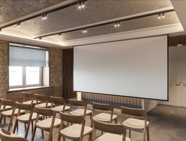 A conference room with a large screen, wooden chairs, brick walls, and a window with blinds.