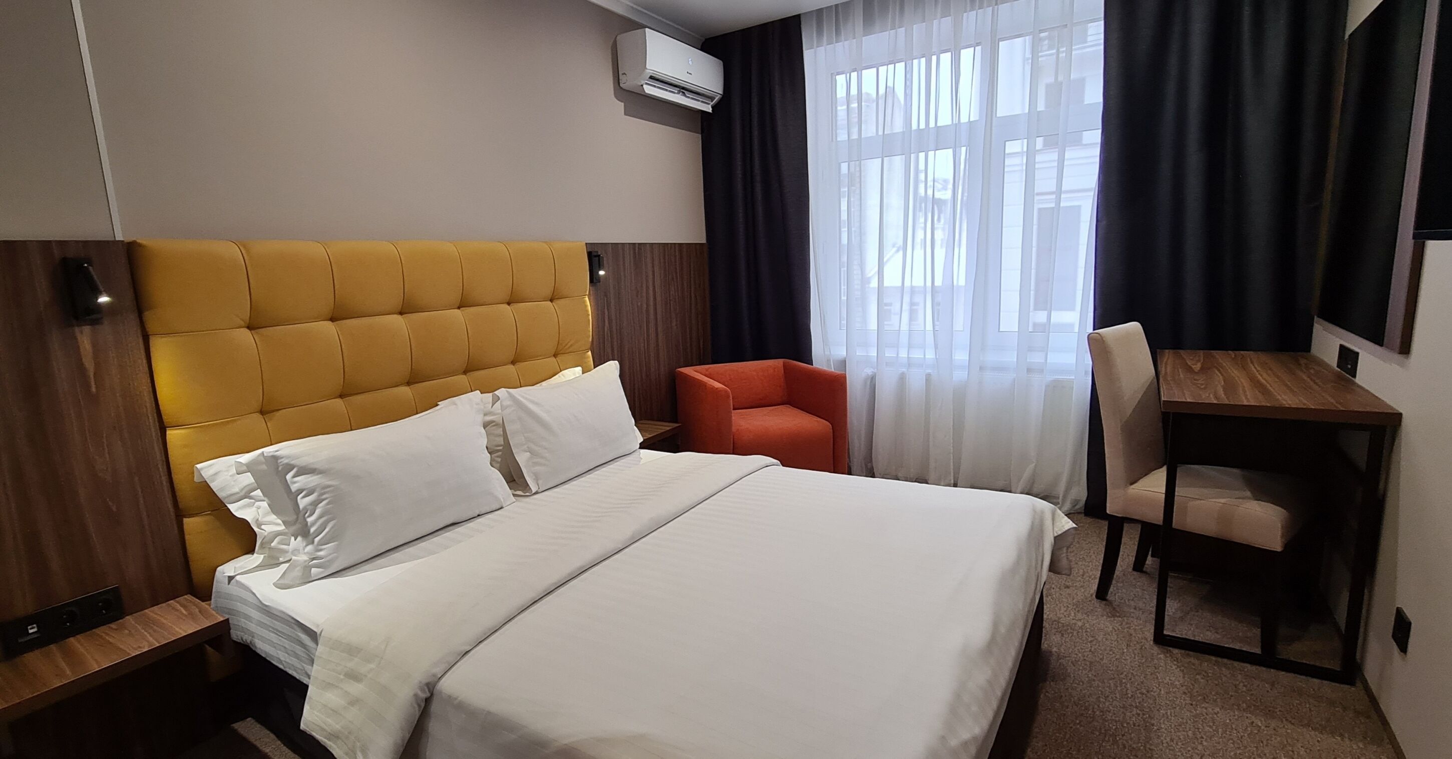 A hotel room with a large bed, a wooden headboard, a desk, and a chair.