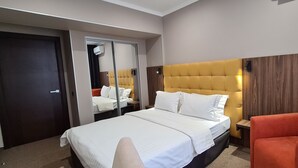 Habitación de hotel con una cama grande, un espejo, un cabecero de madera, un sillón rojo y un panel de pared de madera.