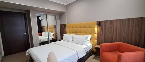 Habitación de hotel con una cama grande, un espejo, un cabecero de madera, un sillón rojo y un panel de pared de madera.