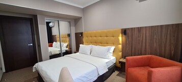 A hotel room with a large bed, a mirror, a wooden headboard, a red armchair, and a wooden wall panel.
