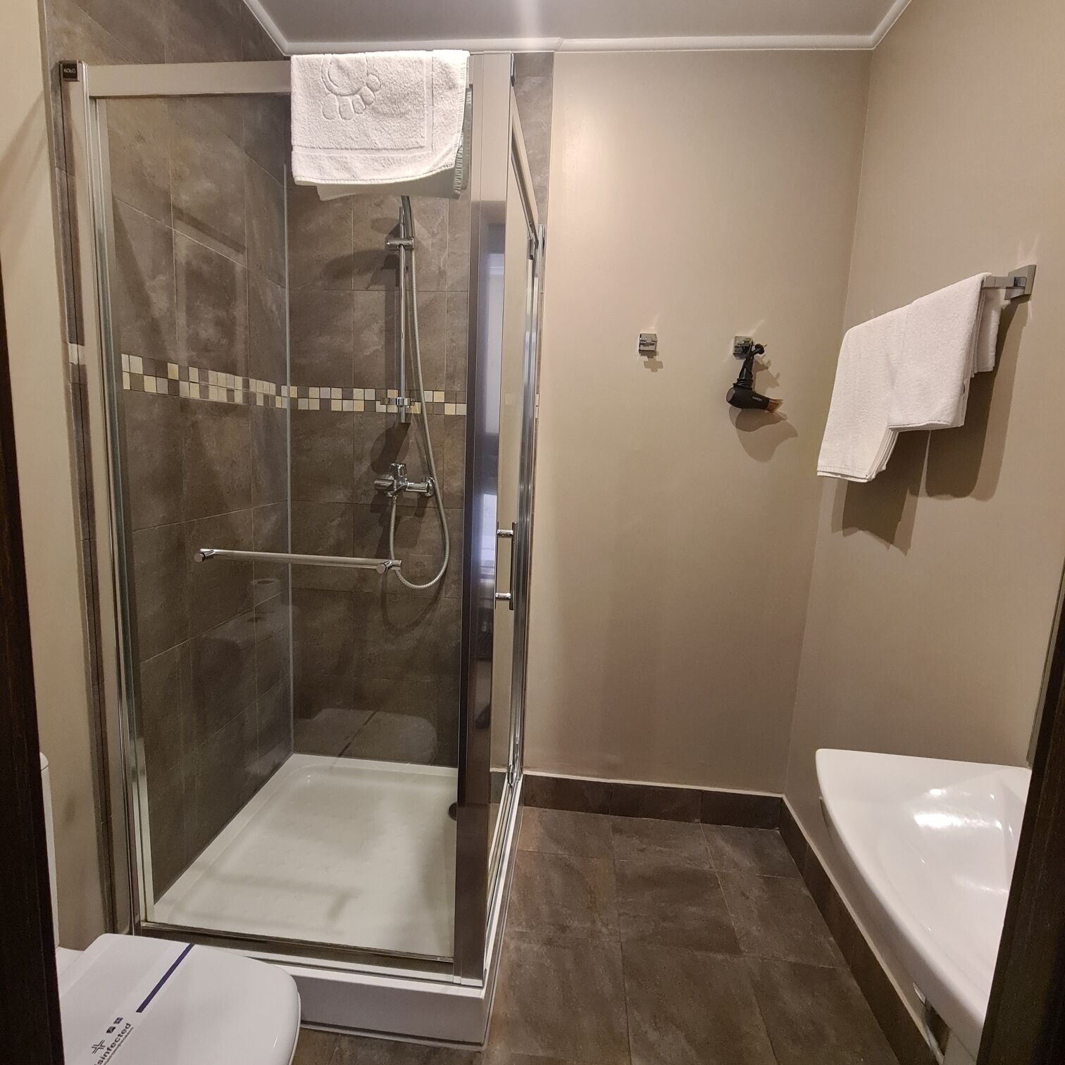 Ducha envuelta en vidrio con cabezal de ducha manual, una toalla colgada en la pared y un lavamanos blanco con espejo.