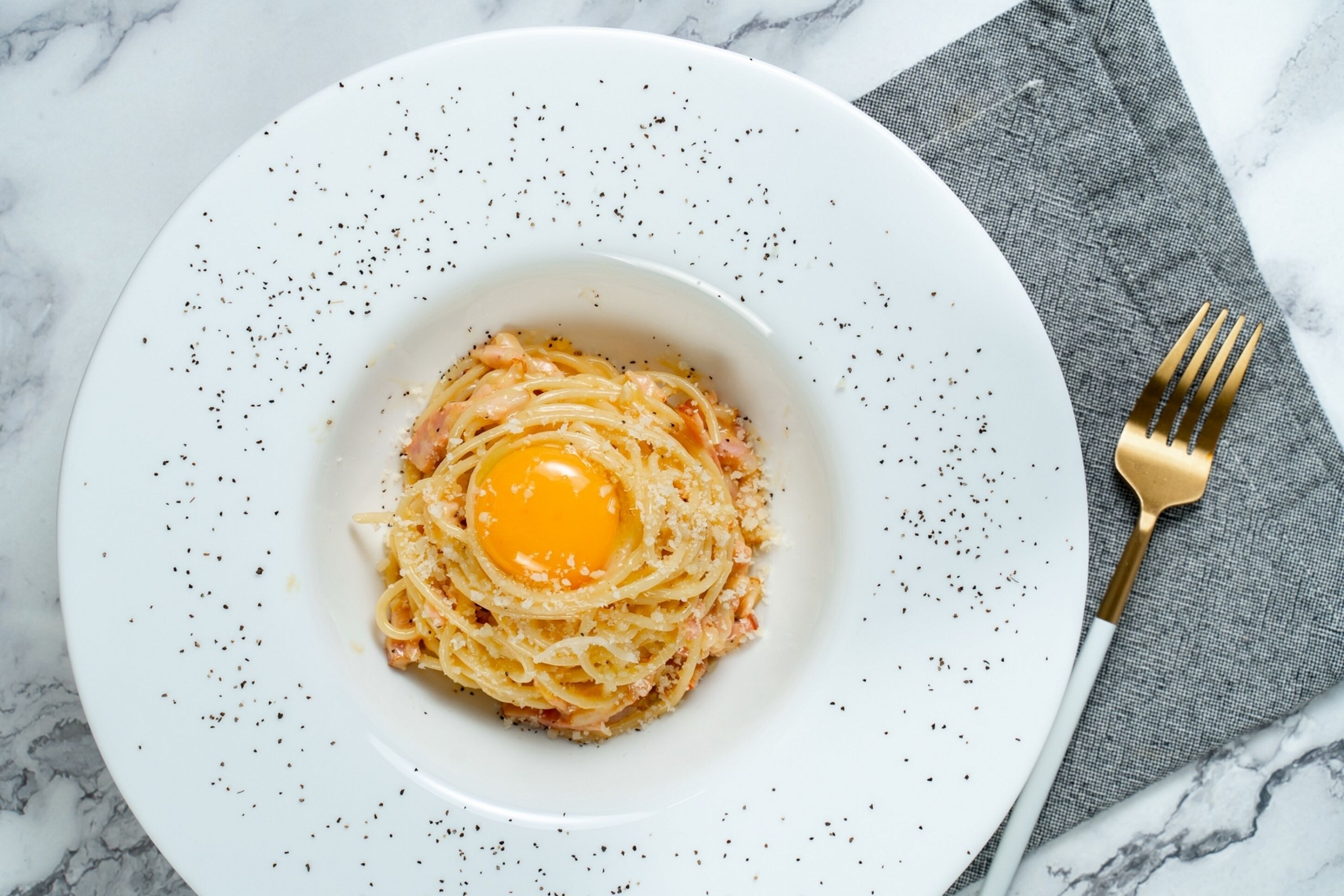 Valkoinen lautanen, jossa on pastaa ja paistettu kananmuna, ja kaikki on asetettu marmoripinnan päälle.