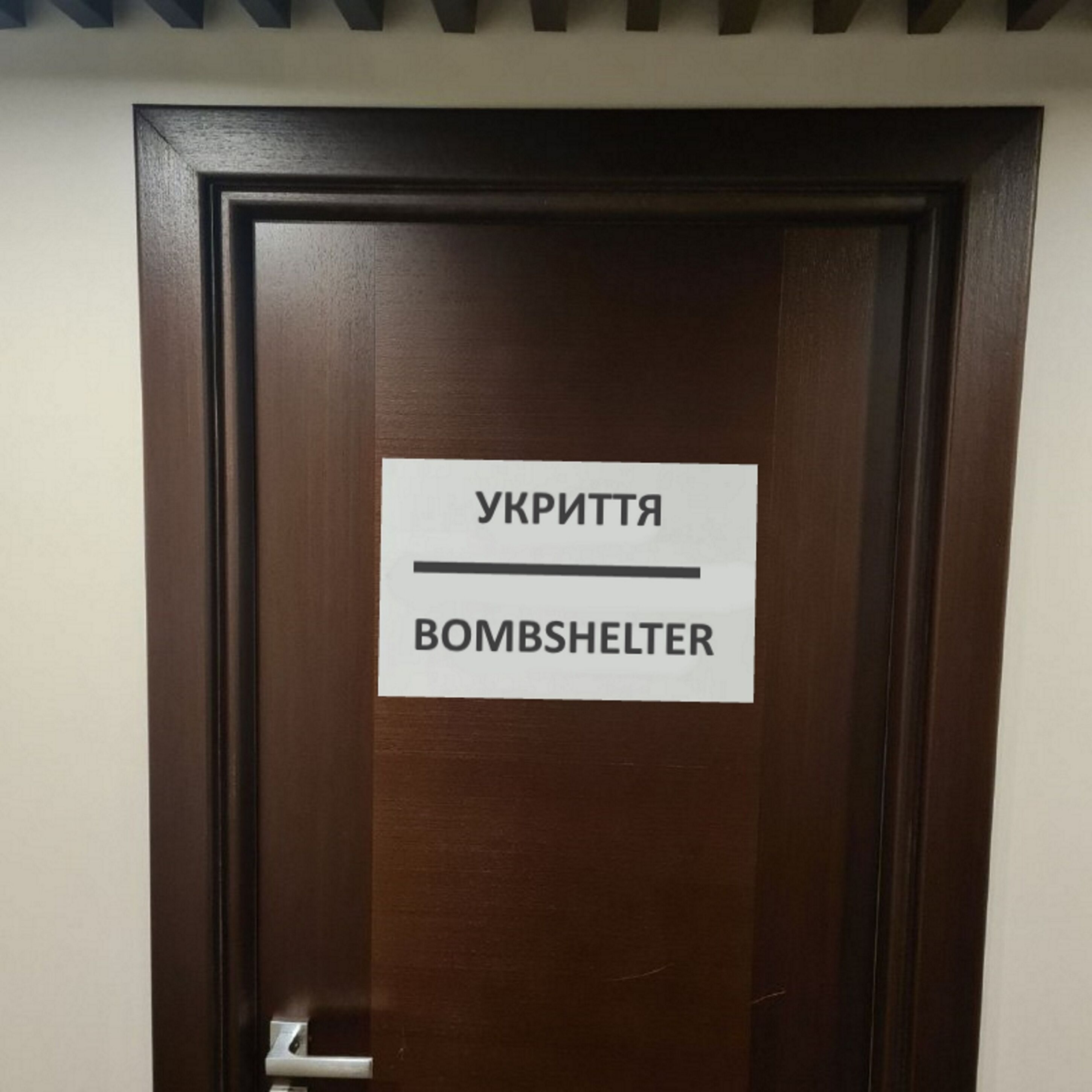 Une porte sur laquelle est affiché un panneau indiquant : « УКРІТТЯ » (abri antiaérien).