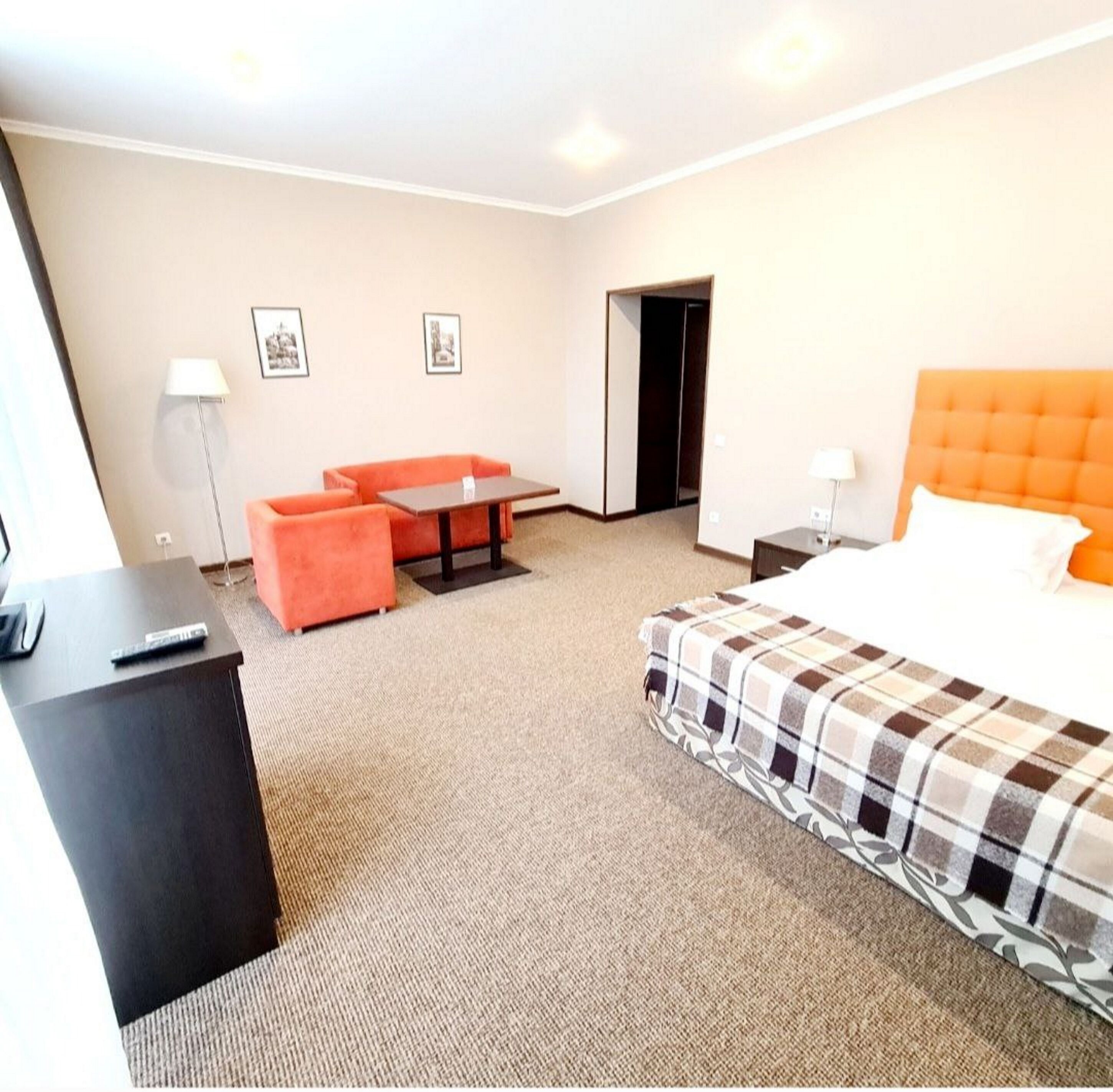 Quarto de hotel com cama, escrivaninha, cadeira, mesa e duas fotografias emolduradas na parede.