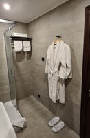 Un baño moderno con cabina de ducha de vidrio, una bañera blanca y un perchero con varias toallas y una bata.