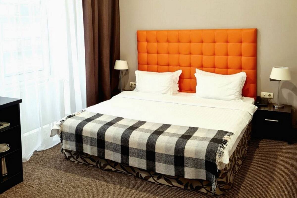 Una habitación de hotel con una cama grande, dos mesitas de noche, una lámpara y un ventanal con cortinas.