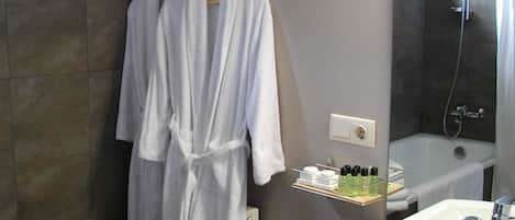 Un baño con una bañera blanca, un lavabo y una ducha. Hay toallas apiladas en el suelo y un soporte con botellas.