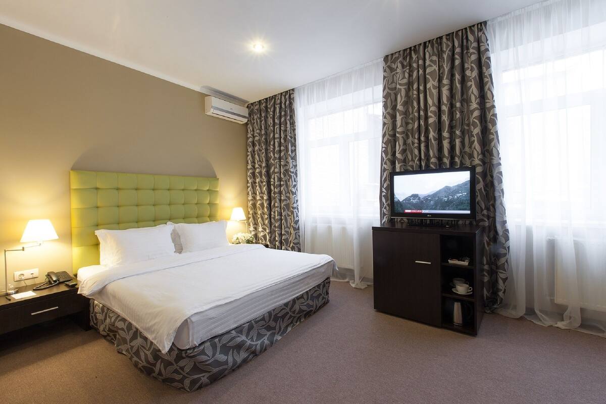 Una habitación de hotel con cama, televisión, mesita de noche y escritorio con lámpara.