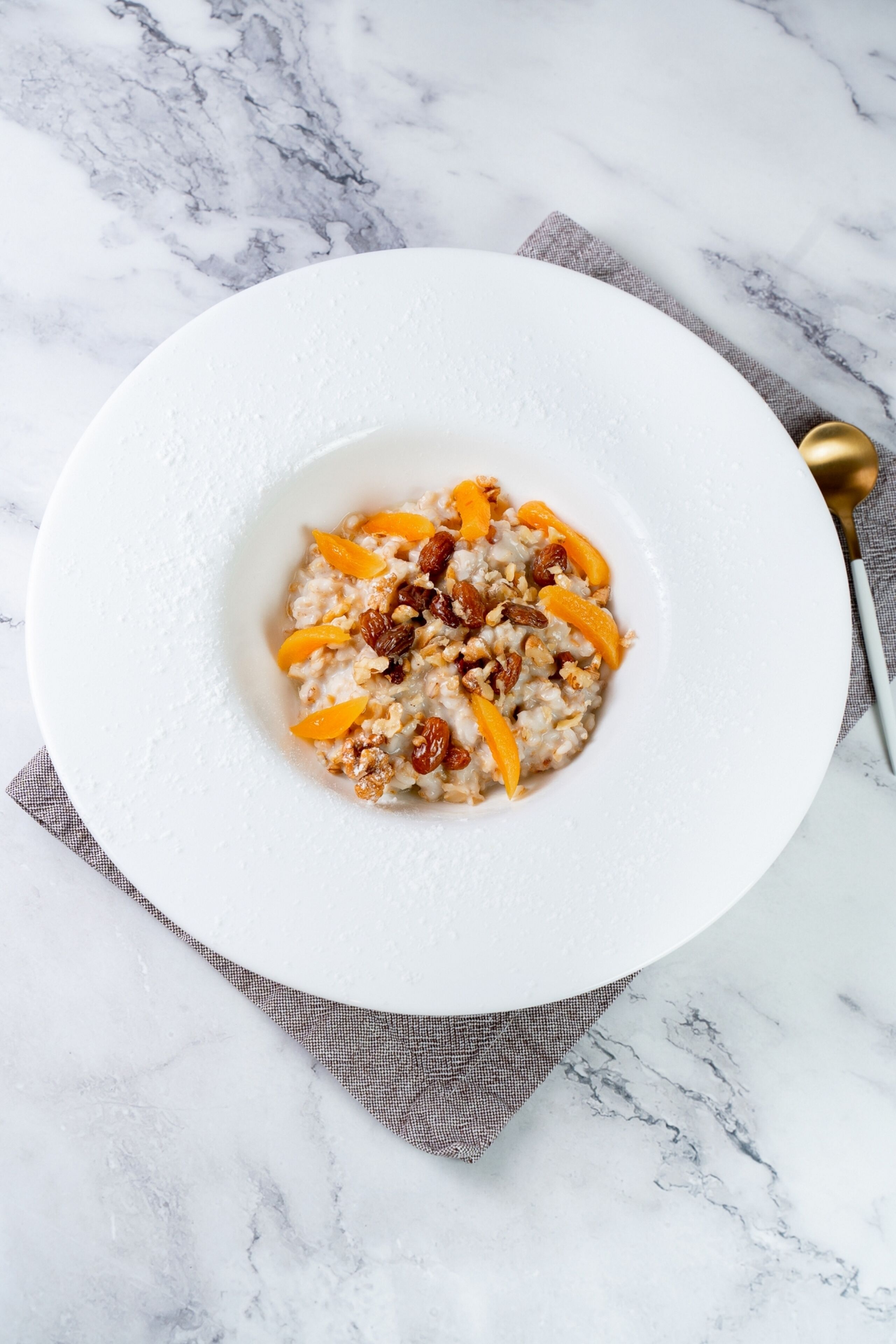 A white bowl of oatmeal with raisins and orange slices on a marble surface.