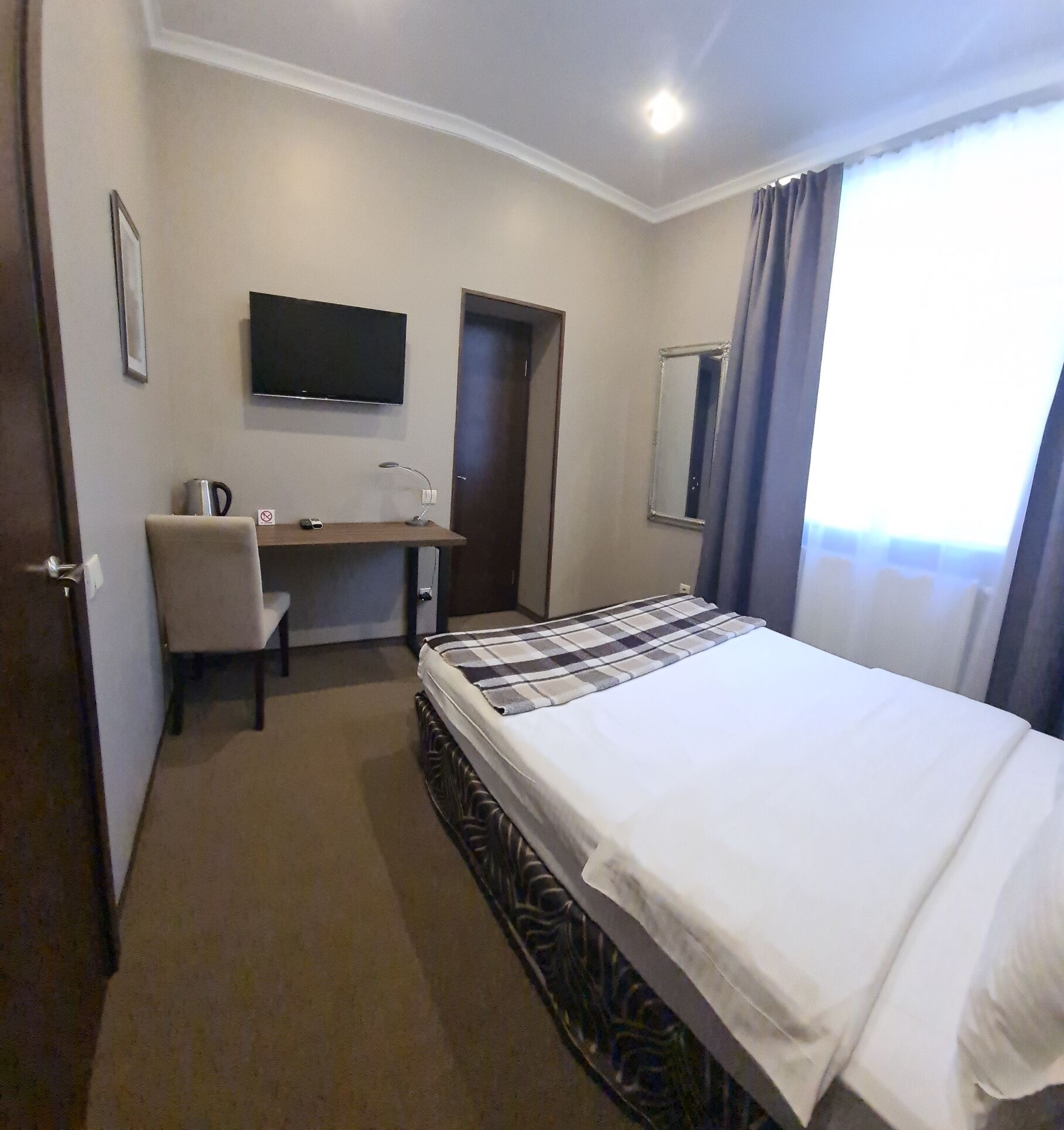 Une chambre d’hôtel équipée d’un lit, d’un bureau, d’une chaise, d’une télévision et d’une fenêtre avec des rideaux.