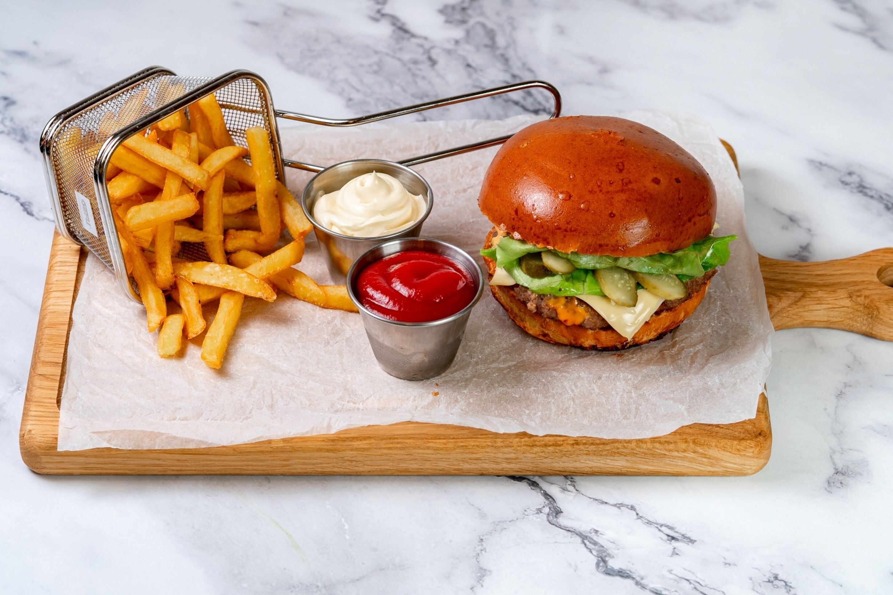 A burger with fries and condiments on a marble surface.
