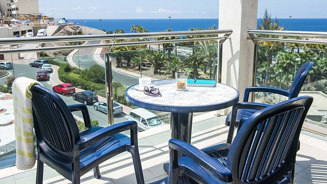 A balcony with two blue chairs, a small round table, and a glass of drink.