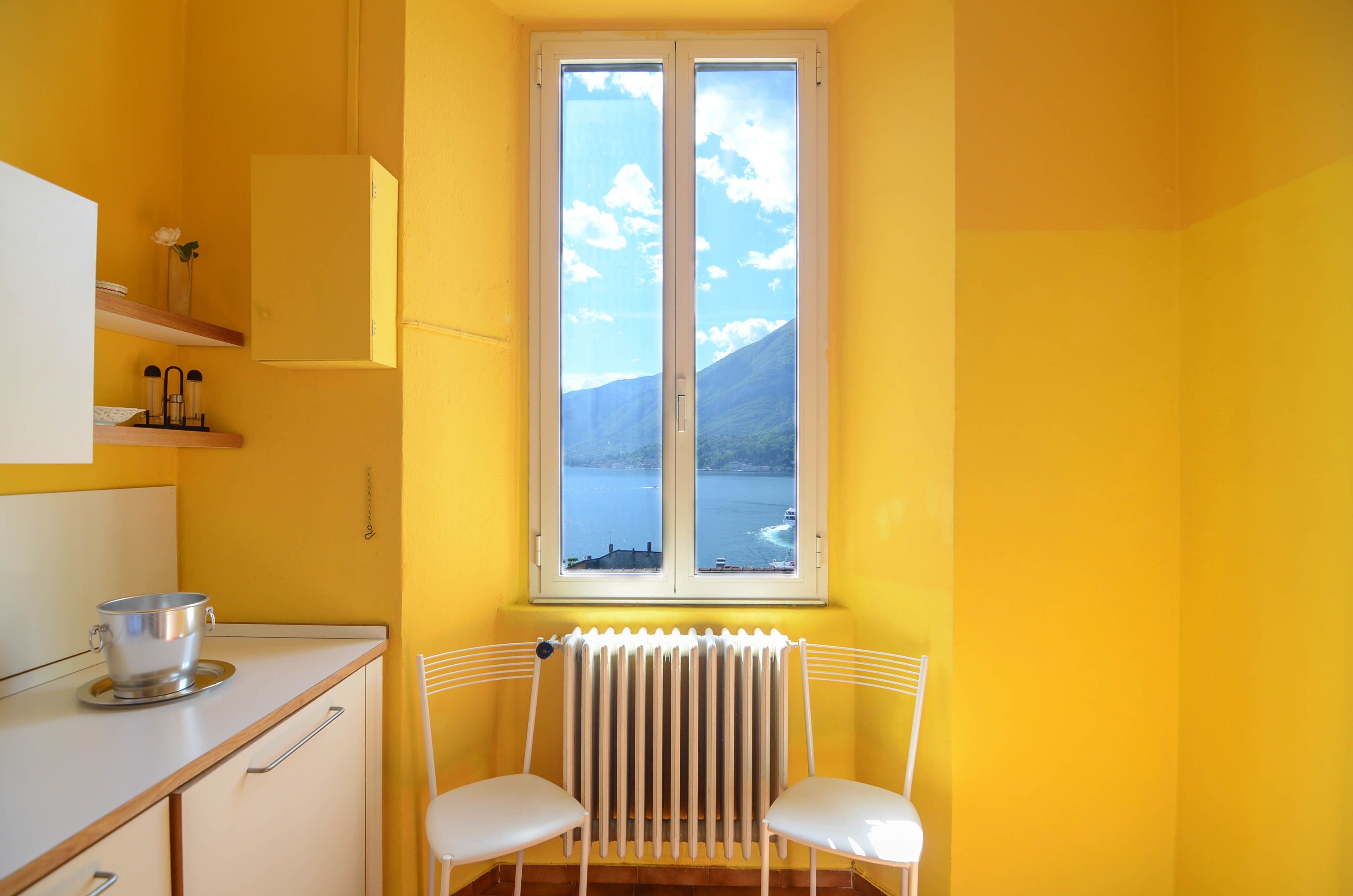 A yellow room with a window, a radiator, a chair, and a table with a pot.