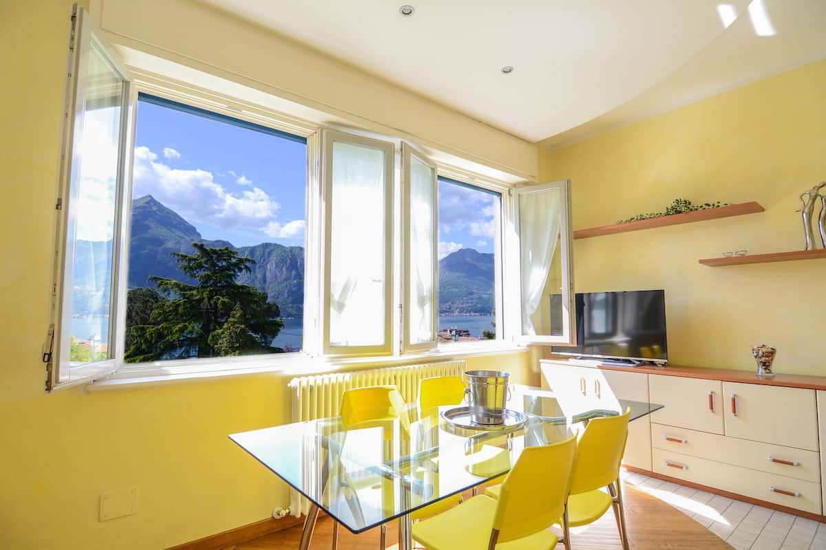 A bright room with a table and chairs, a television, and a view of mountains through large windows.