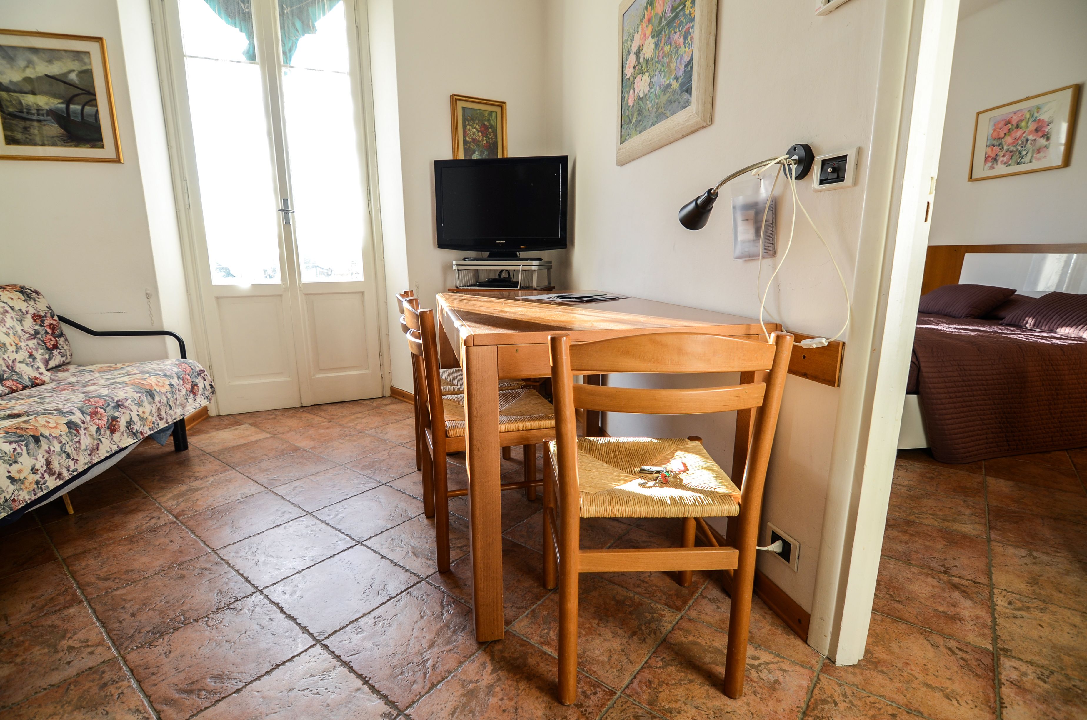 Una stanza con un tavolo da pranzo in legno, sedie, una televisione e un letto con coperta marrone.