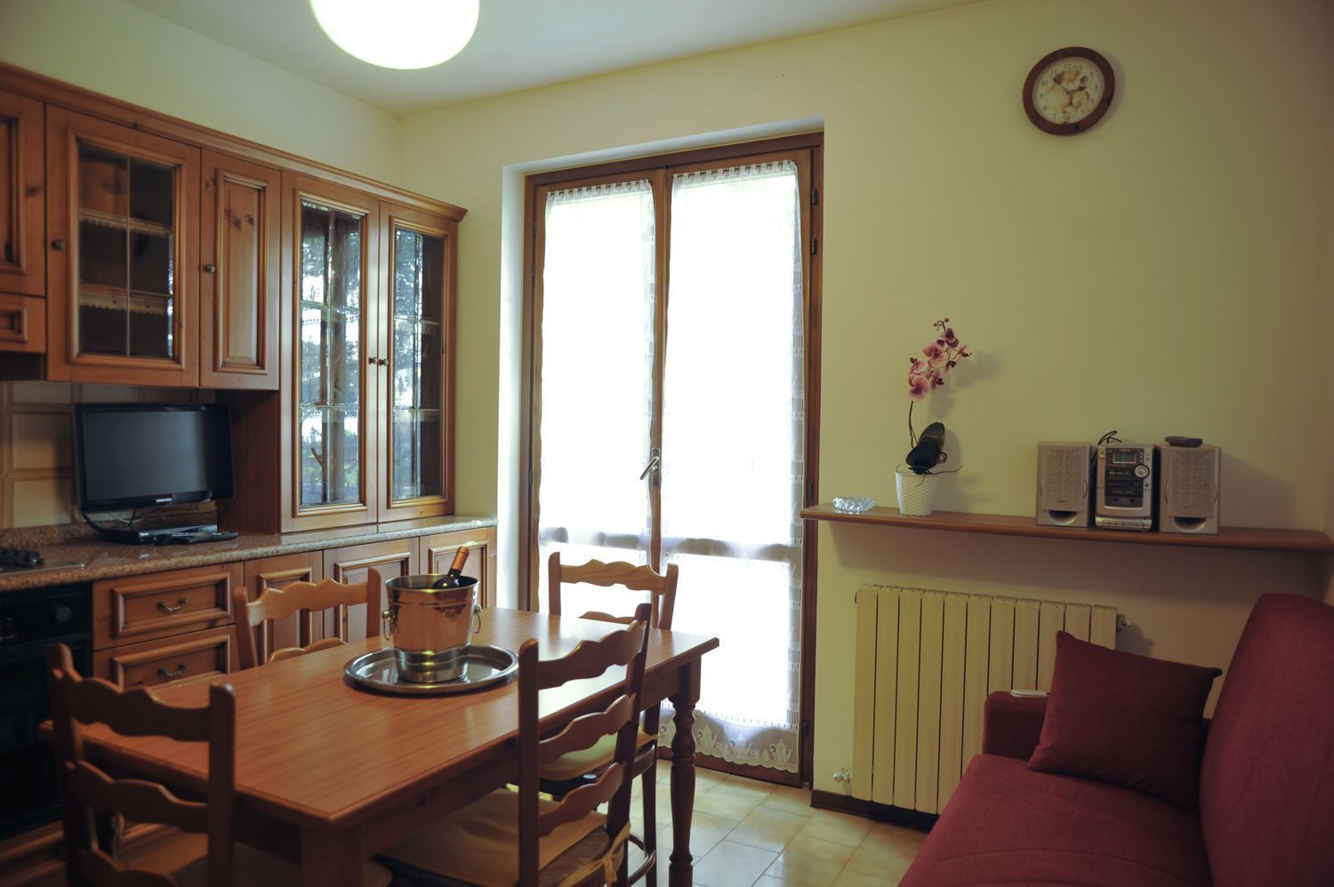 A kitchen with wooden cabinets, a dining table with chairs, a television, and a window with curtains.