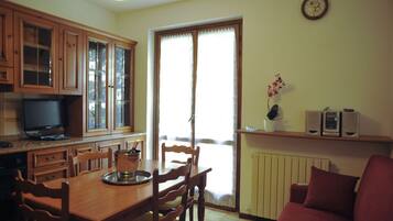 A kitchen with wooden cabinets, a dining table with chairs, a television, and a window with curtains.