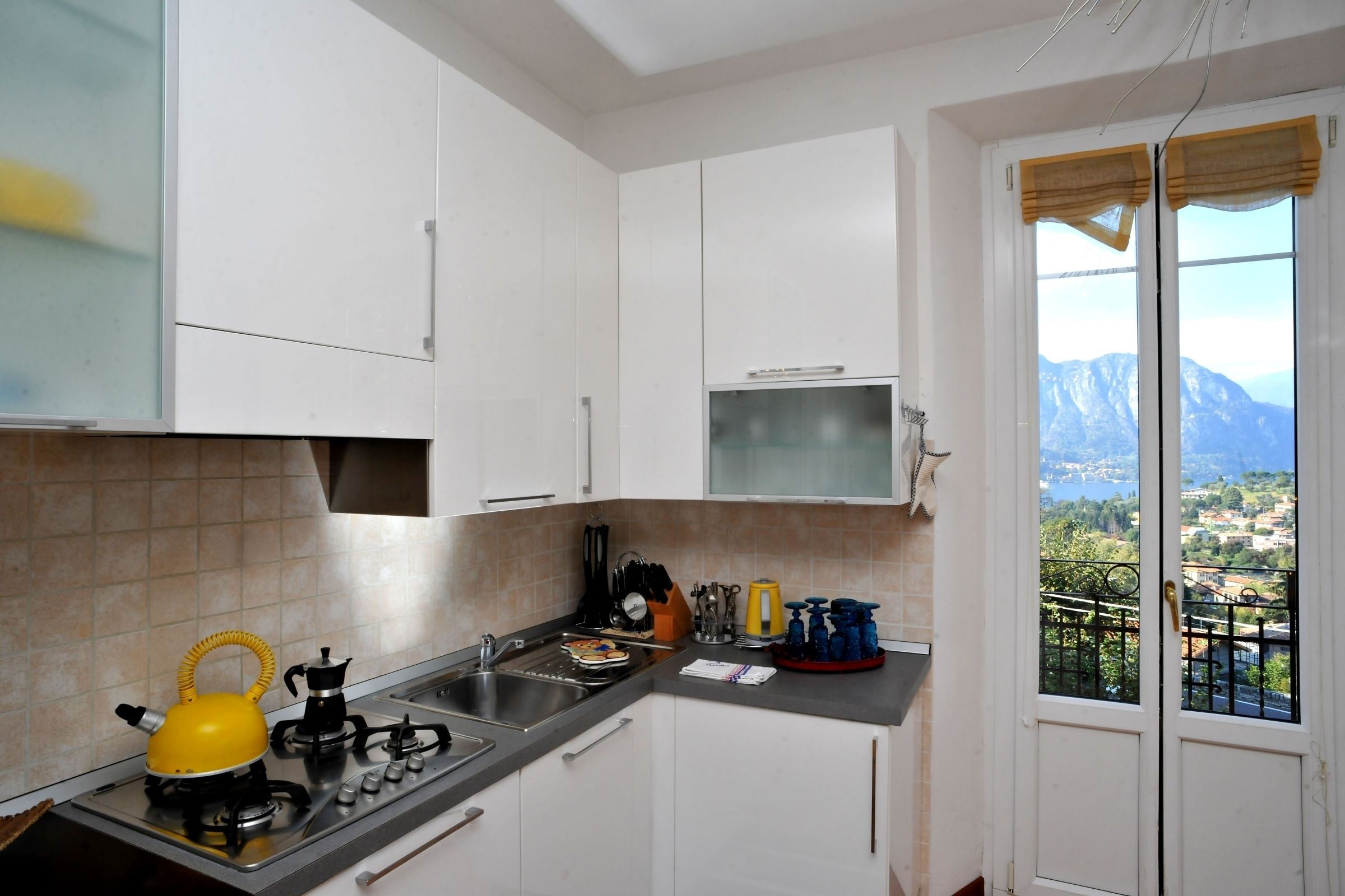A kitchen with white cabinets, a gas stove, a kettle, and a window with a view of mountains.