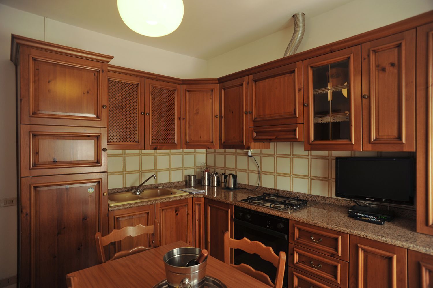 Une cuisine avec des meubles en bois, un plan de travail en granit, une cuisinière à gaz, un évier et une table à manger avec des chaises.