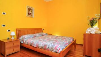 A bedroom with a wooden bed, a nightstand with a lamp, a dresser, and a framed picture on the wall.