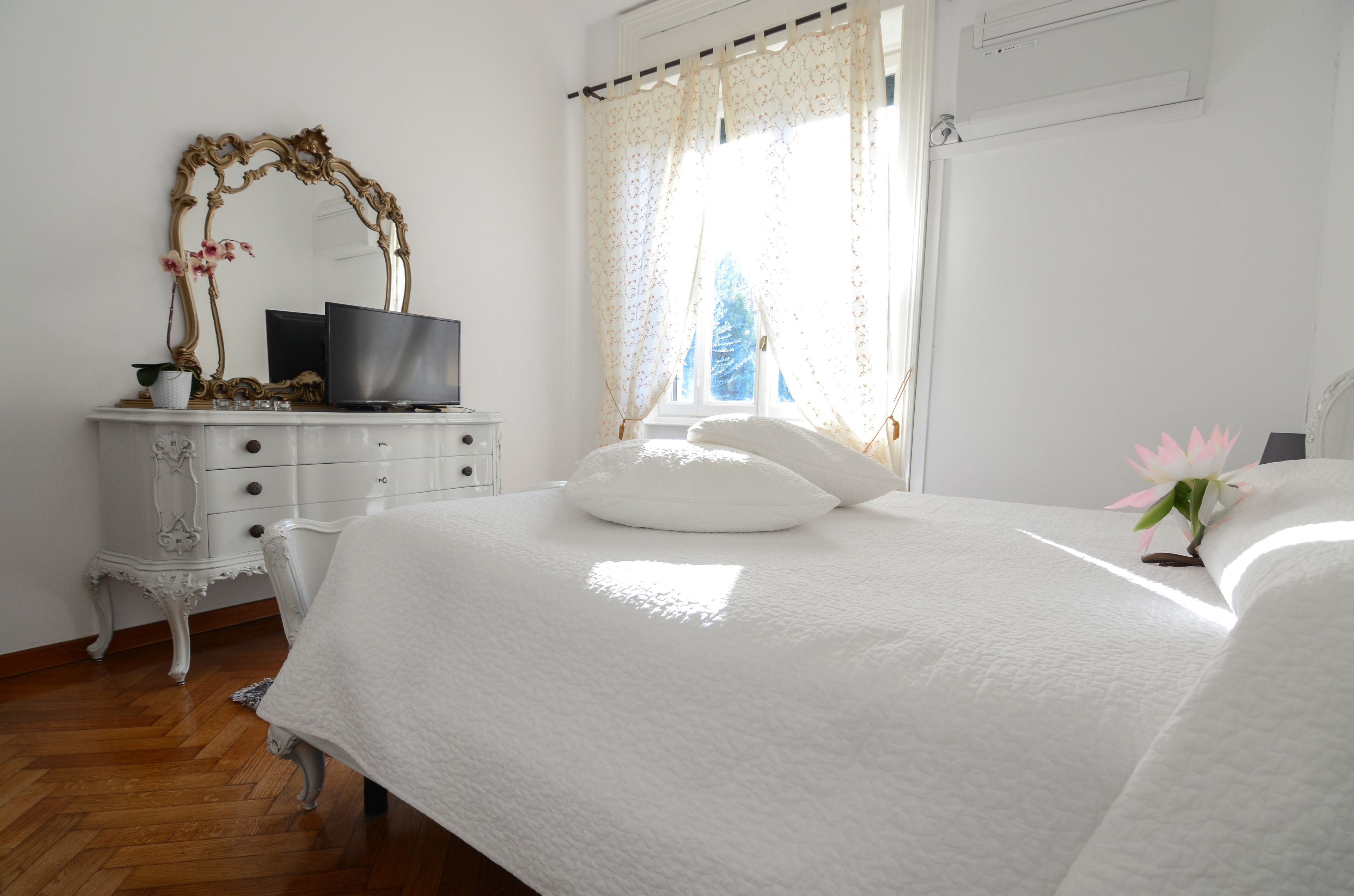 A bedroom with a bed, a dresser, a TV, and a window with curtains.