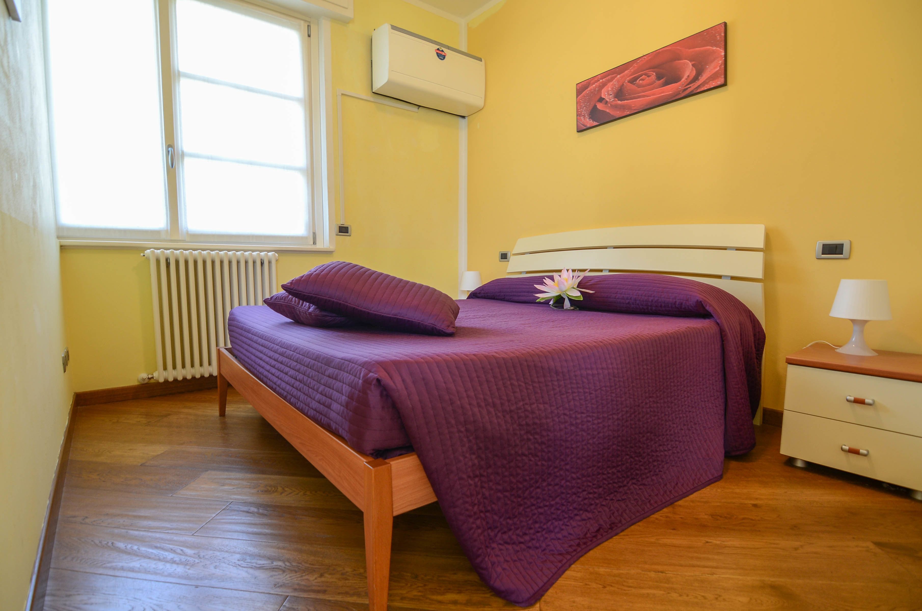 Une chambre à coucher avec un lit en bois, un radiateur, une fenêtre et un climatiseur fixé au mur.