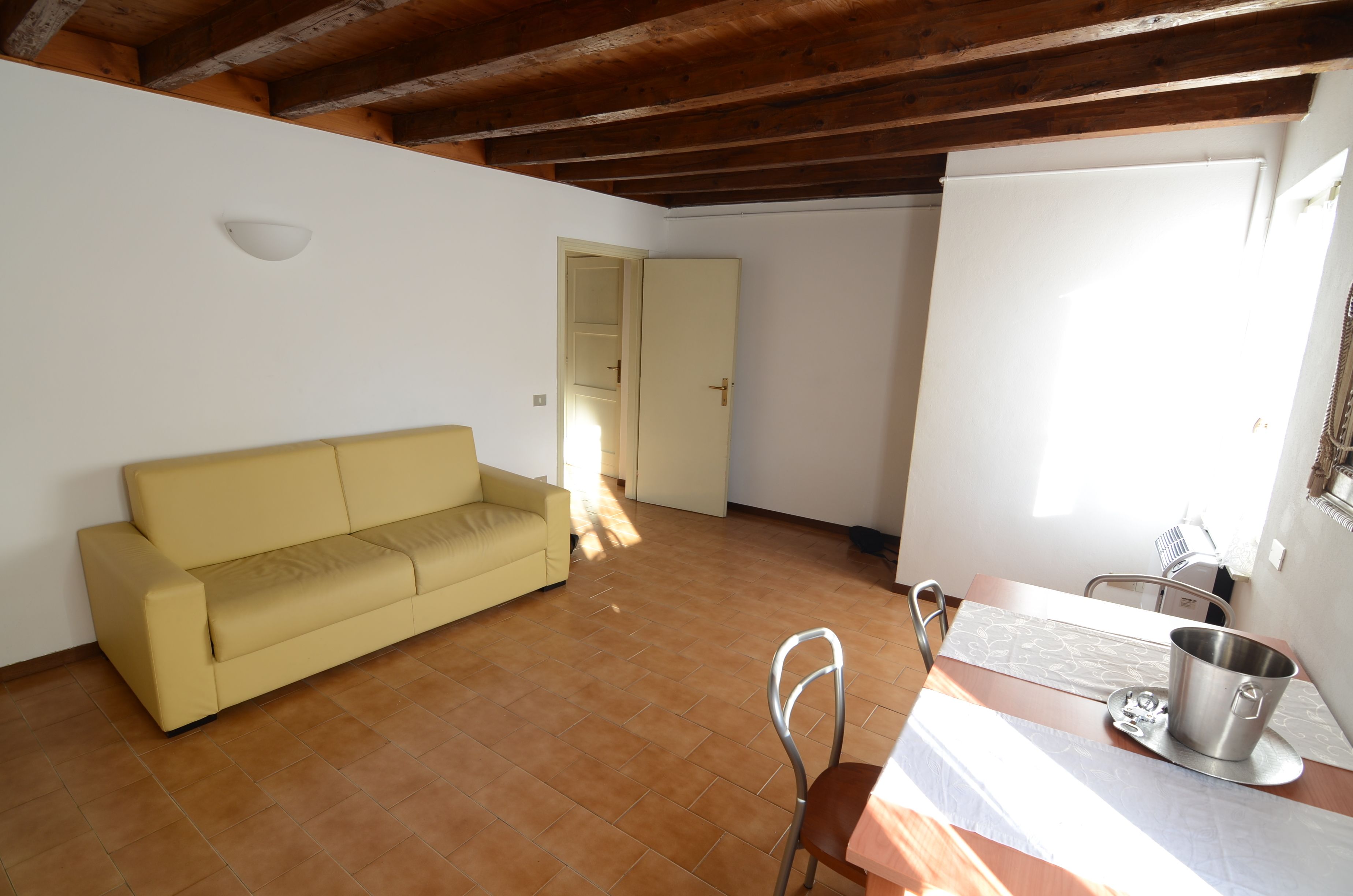 A room with a yellow sofa, a dining table with chairs, a metal pot, and a wooden ceiling.