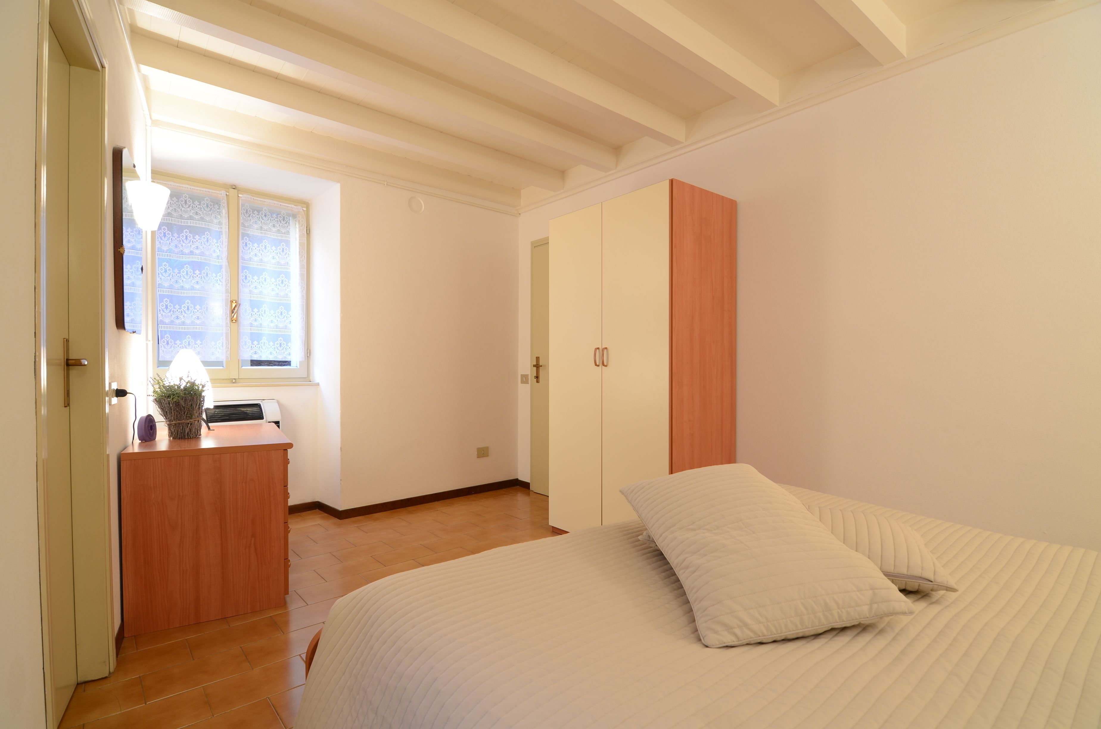 A bedroom with a bed, a wooden dresser, a window with patterned curtains, and a door.