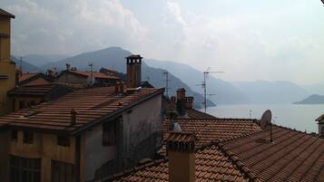 Blick auf terrakotta-gedeckte Dächer mit Schornsteinen, Satellitenschüsseln und Antennen, mit Blick auf ein Gewässer und ferne Berge.