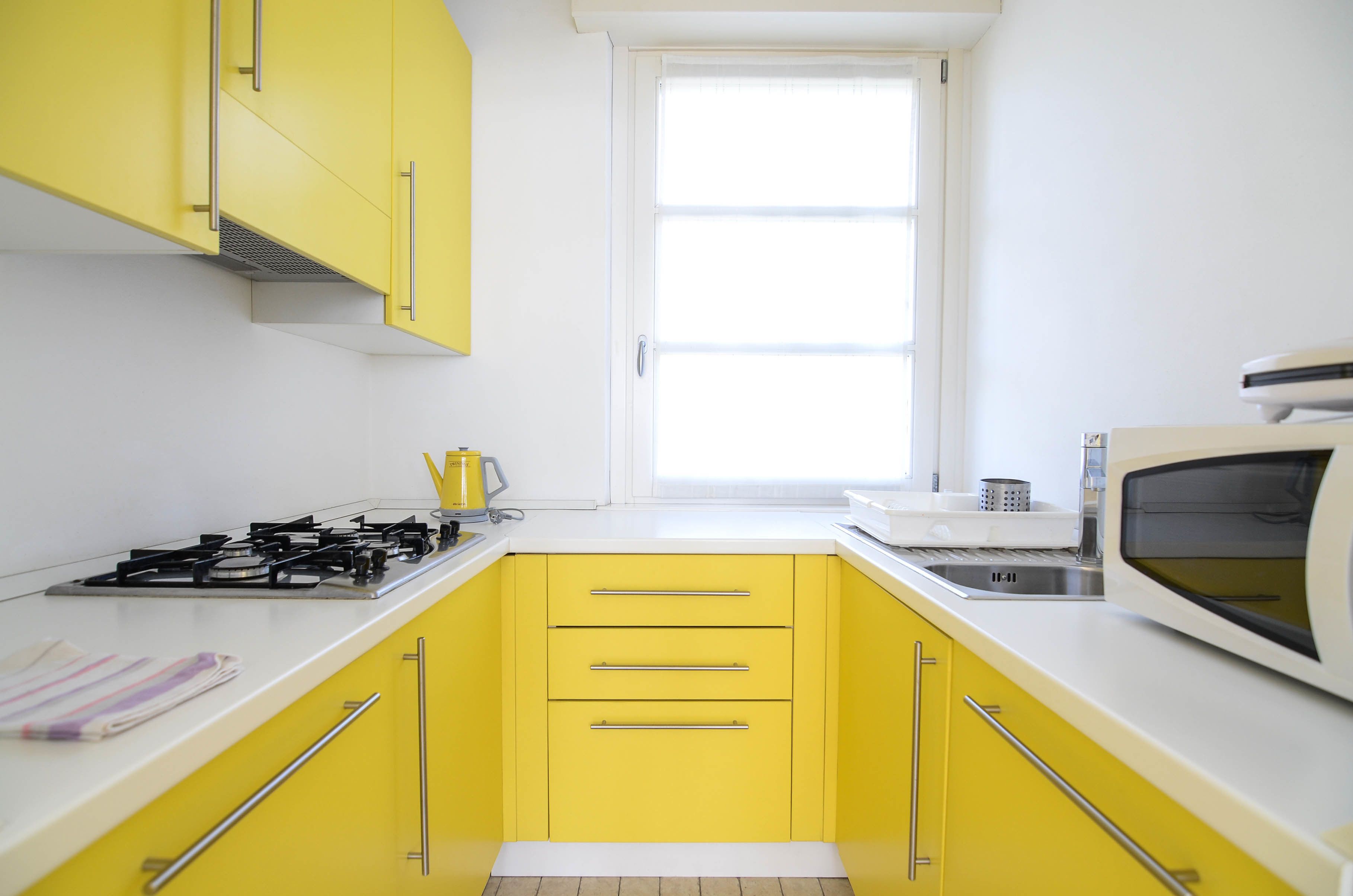 Una cocina con gabinetes amarillos, estufa a gas, microondas y ventana.