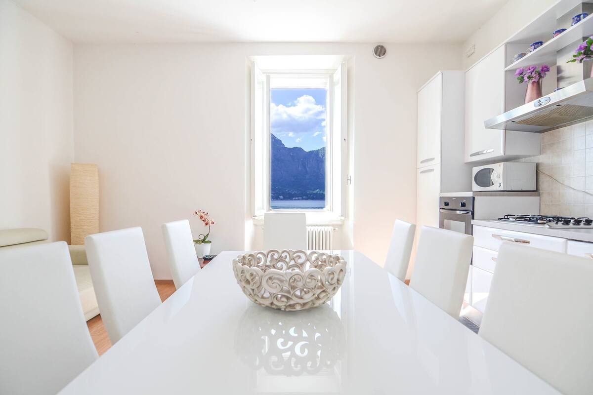 A modern kitchen with white cabinetry, a dining table with chairs, and a view of mountains through a window.