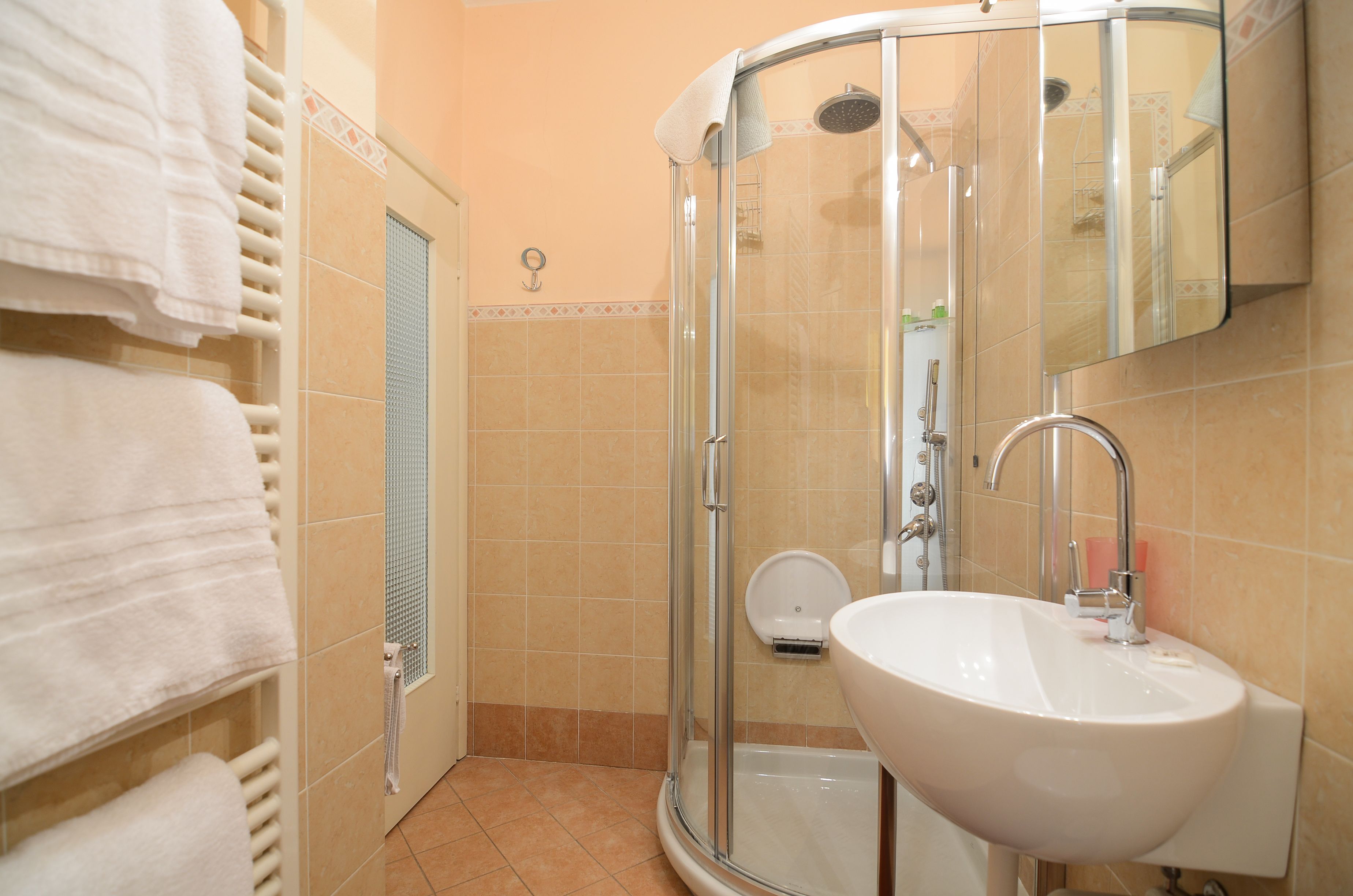 Un baño con cabina de ducha de vidrio, un lavamanos blanco y un perchero con toallas dobladas.