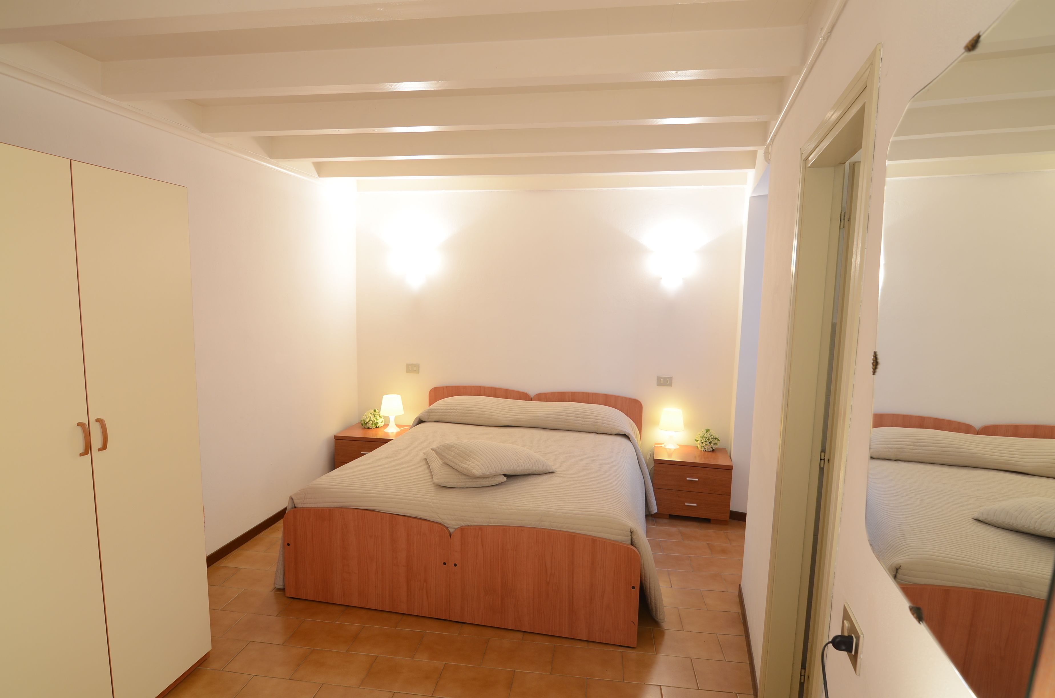 A bedroom with a wooden bed, bedside tables with lamps, and a wardrobe.