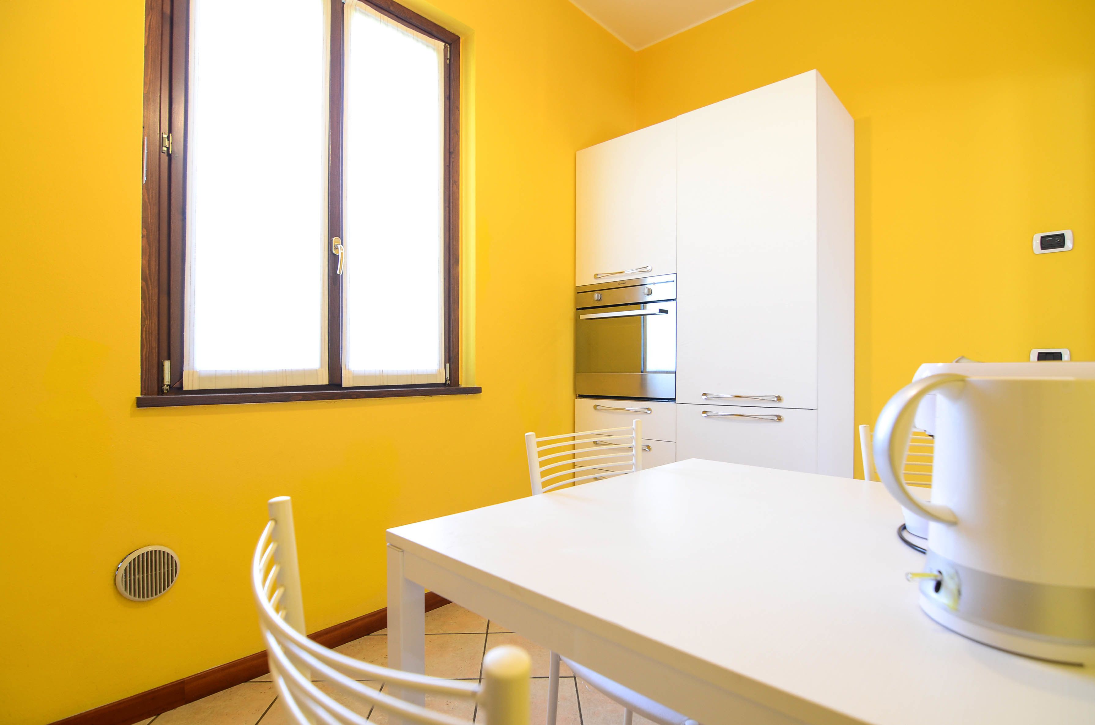 A bright yellow kitchen with white cabinets, a stainless steel oven, and a white table with a kettle.