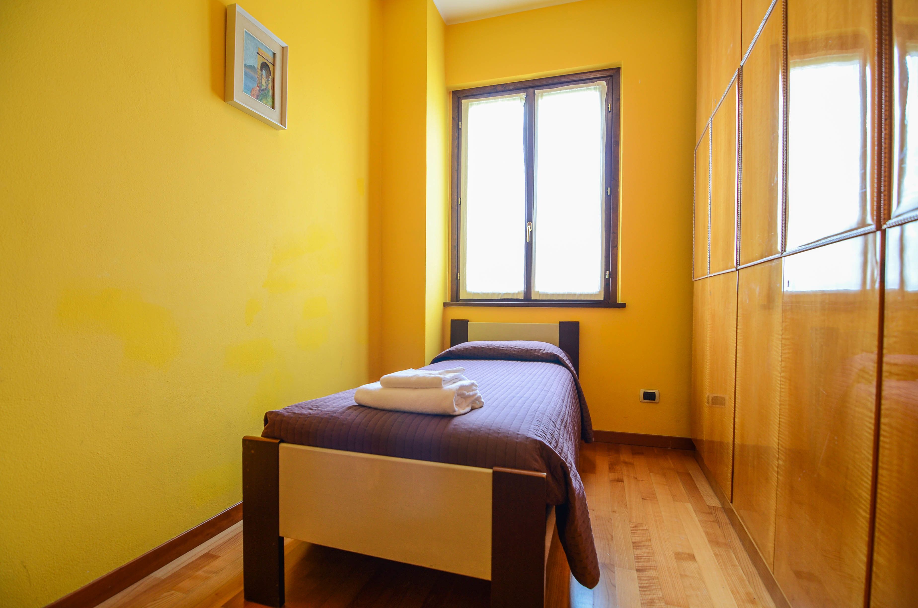 A small, bright room with a bed, a window, and a wardrobe.