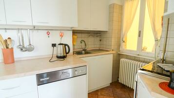 A kitchen with white cabinets, a dishwasher, a kettle, and a window with curtains.