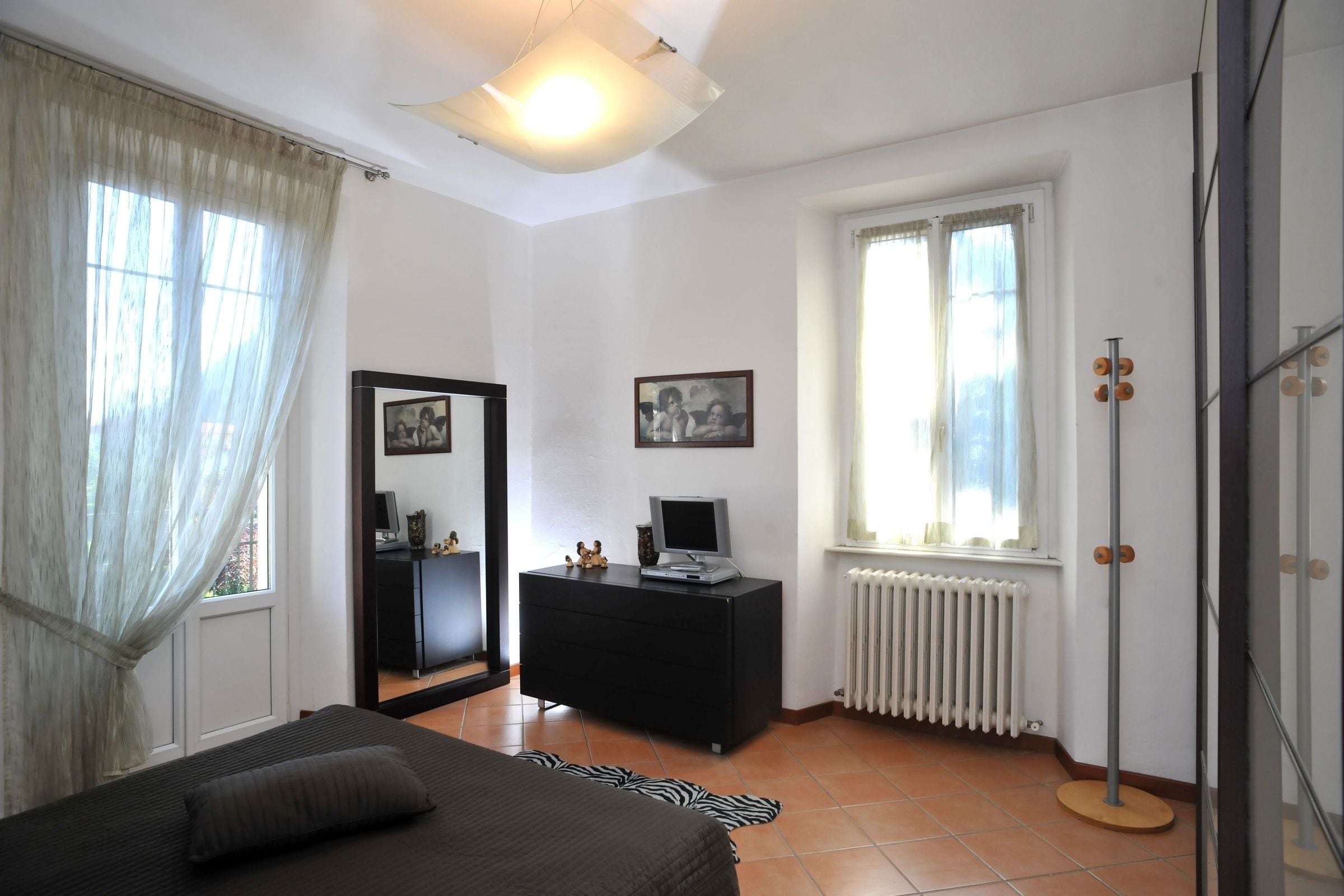 Un dormitorio con cama, cómoda, espejo y radiador.