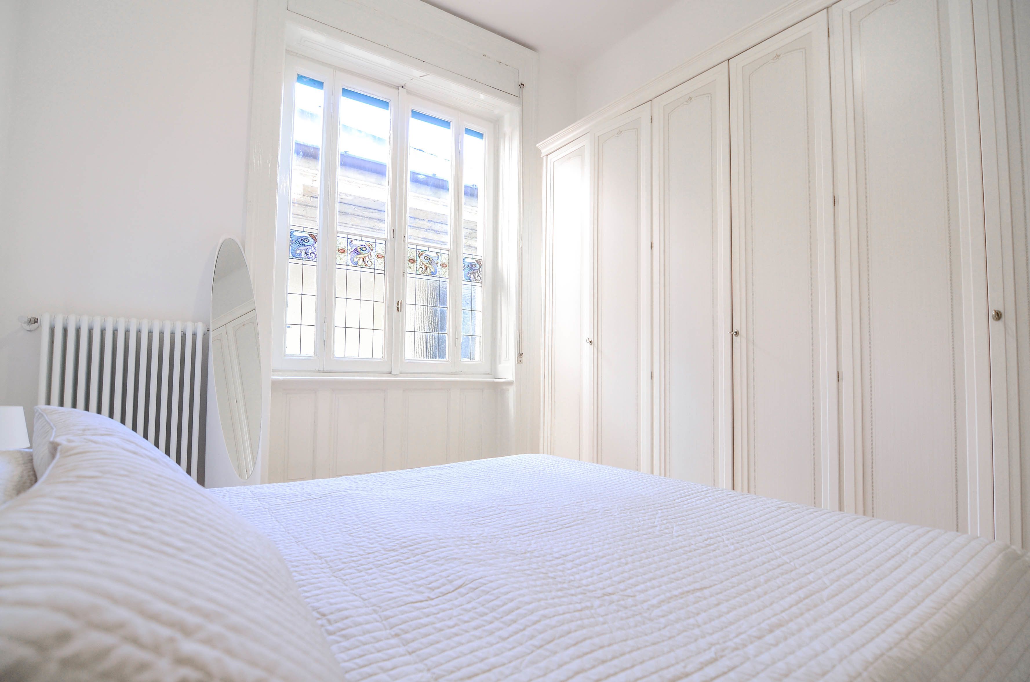 Een slaapkamer met een groot bed, een radiator, een raam met uitzicht en witte kasten.