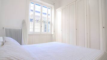 Een slaapkamer met een groot bed, een radiator, een raam met uitzicht en witte kasten.