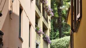 En smal kullerstensgata med byggnader på båda sidor, och varje byggnad har balkonger som är dekorerade med hängande blomkorgar.
