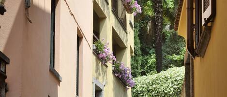 Una stretta strada acciottolata fiancheggiata da edifici con balconi decorati da cesti di fiori pendenti.
