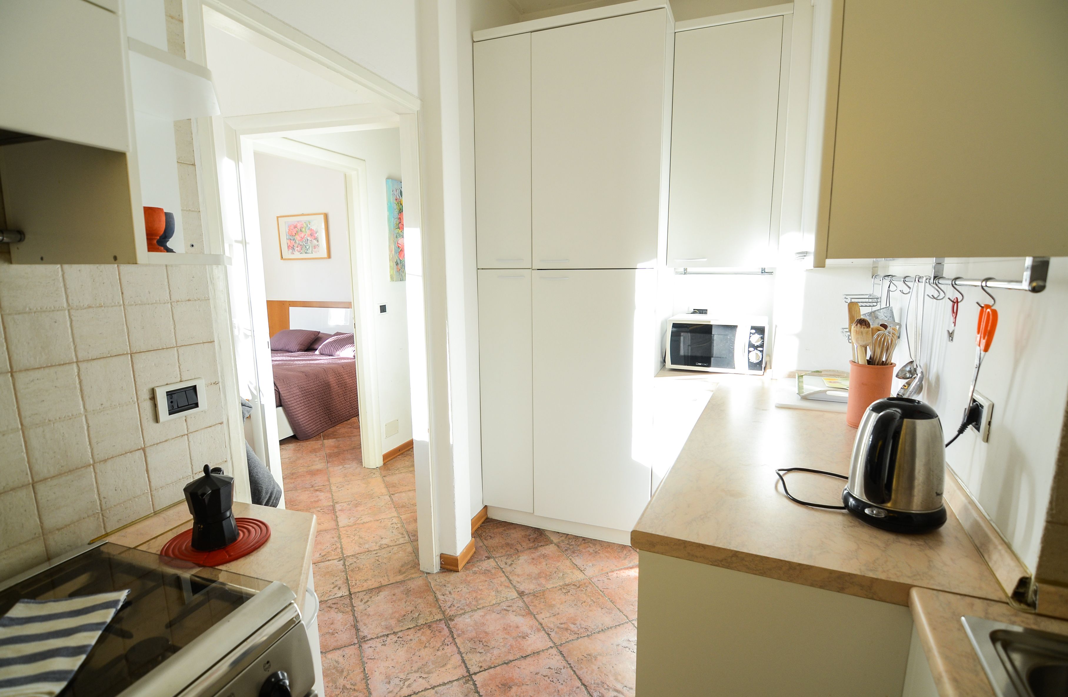 A kitchen with white cabinets, a microwave, and a kettle on the counter.