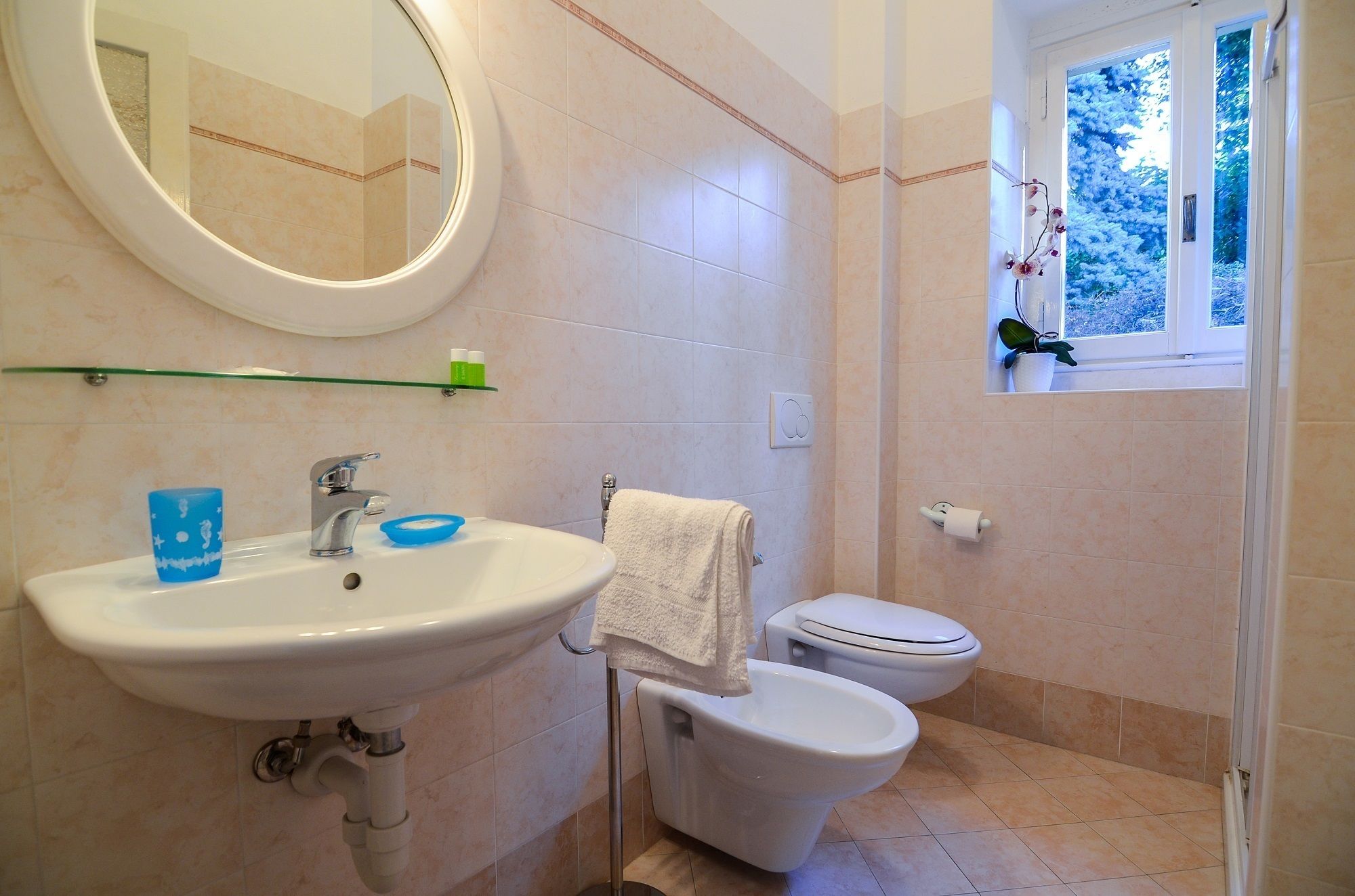 A bathroom with a sink, mirror, toilet, and a window with a view of trees.