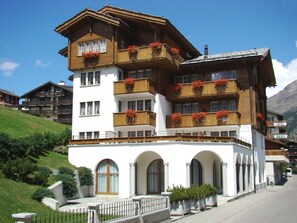 A multi-story hotel with balconies adorned with red flowers, arched windows, and a white facade. - Arcade Apartments (Saas-Fee)