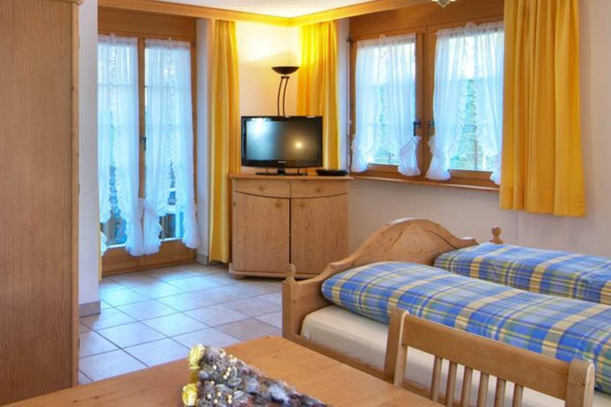 A room with a bed, a TV, a wooden cabinet, and a window with curtains.