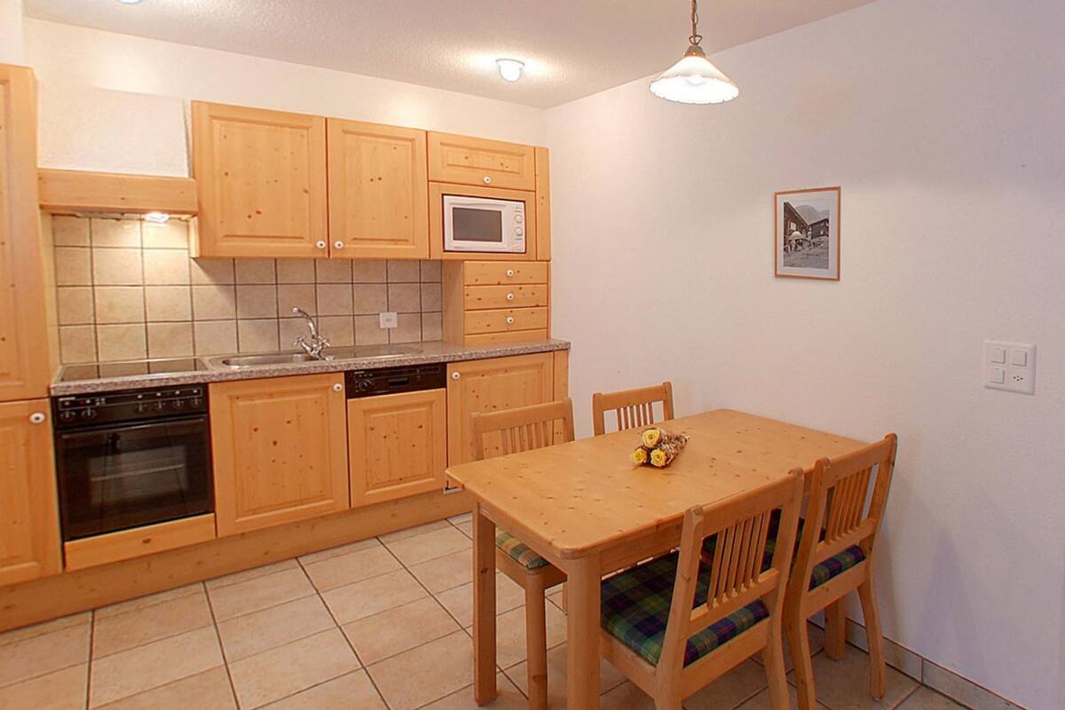 A compact kitchen with wooden cabinets, a built-in microwave, and a dining table with chairs.